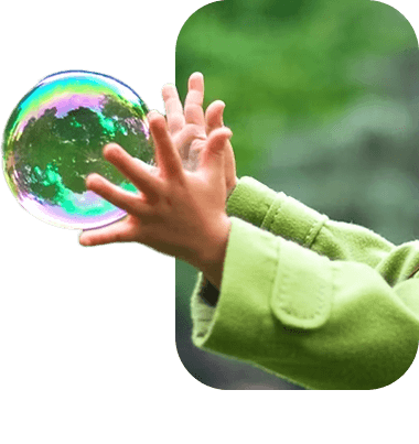 Child's hands reaching for a soap bubble outdoors